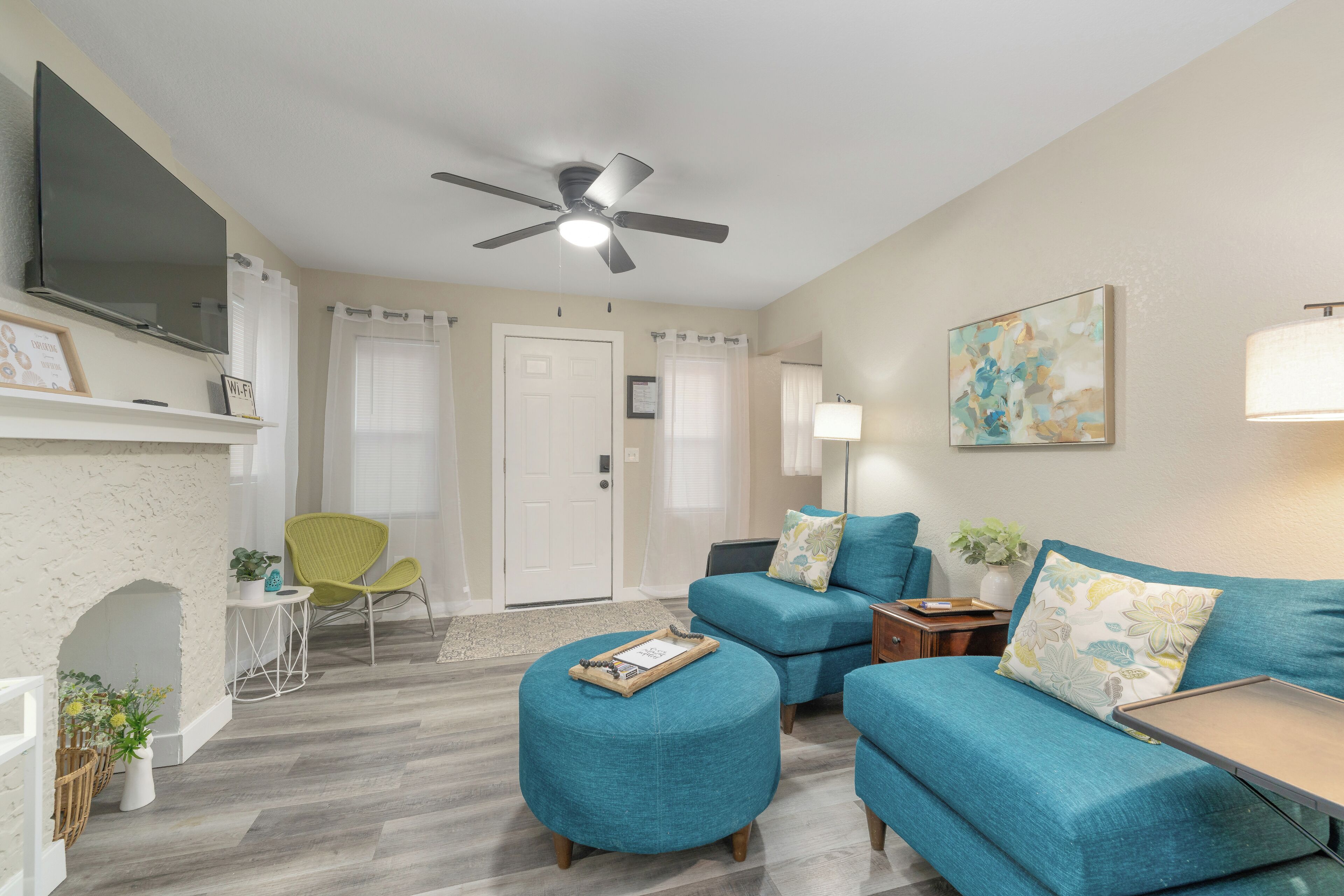 A living room with teal sofas, a white fireplace, a ceiling fan, and a flat-screen TV mounted above the fireplace.