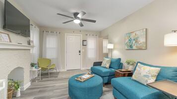 A living room with teal sofas, a white fireplace, a ceiling fan, and a flat-screen TV mounted above the fireplace.