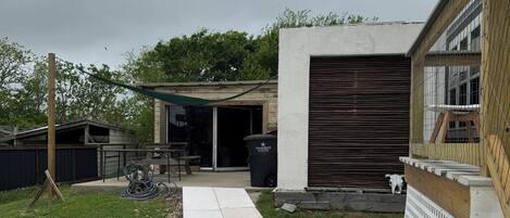 Un sendero de concreto que lleva a un garaje con una persiana cerrada, una valla de madera y una zona verde con rocas dispersas.