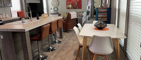 Una cocina moderna con una isla central, taburetes de bar y un comedor con mesa y sillas.