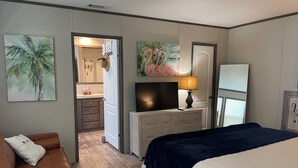 Un dormitorio con cama, televisor, cómoda y puerta que da a un baño.