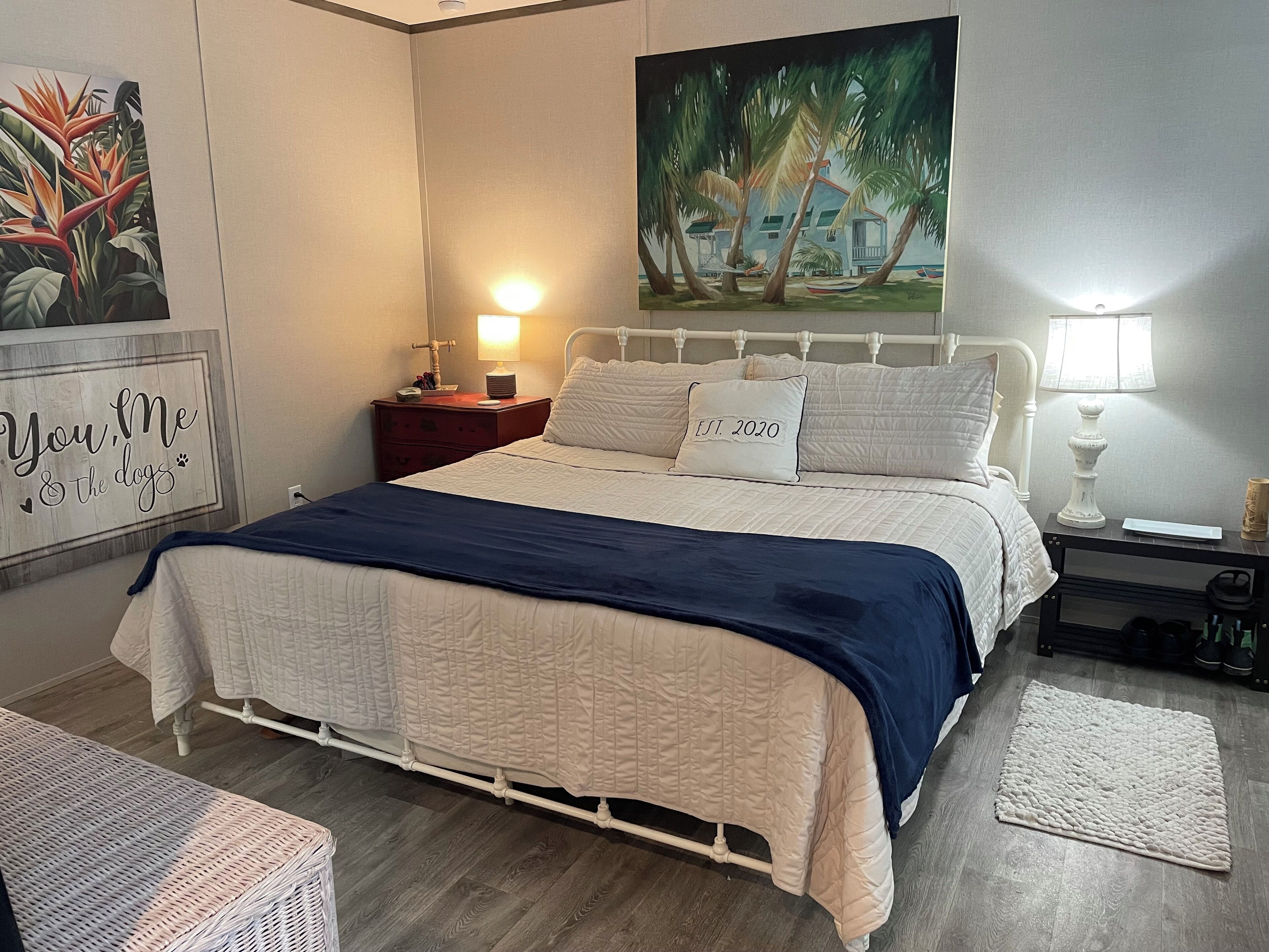 Un dormitorio ordenado con cama, mesitas de noche, lámpara y un cuadro en la pared.