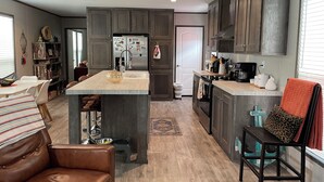 Cocina moderna con armarios de madera oscura, una isla central y un comedor con sofá de cuero y mantel a rayas.