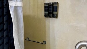 Um banheiro com área de chuveiro, porta-toalhas e três frascos de produtos de higiene no muro.