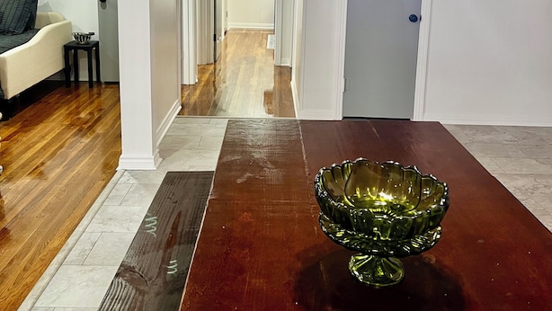 Uma sala de jantar com uma mesa de madeira, uma tigela de vidro verde e um corredor que dá para outro quarto.