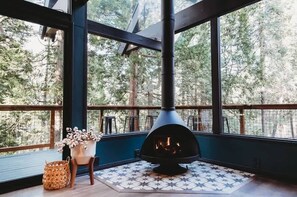 A modern interior with a large fireplace, a view of trees through large windows, and a patterned floor.