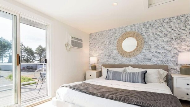 A bedroom with a large bed, a wall-mounted mirror, and a view through a sliding glass door. - Ocean Boulevard South, 3 min walk to the beach! (Rye)
