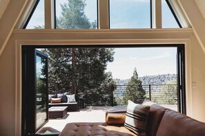 Quarto com uma grande porta de vidro deslizante que dá para uma área externa com espaço para sentar e vista para árvores e colinas.