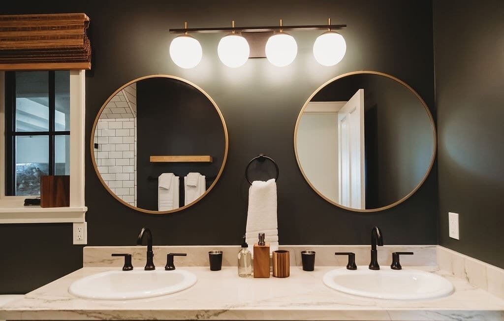 A bathroom with two sinks, round mirrors, a towel rack, and a window with a view.