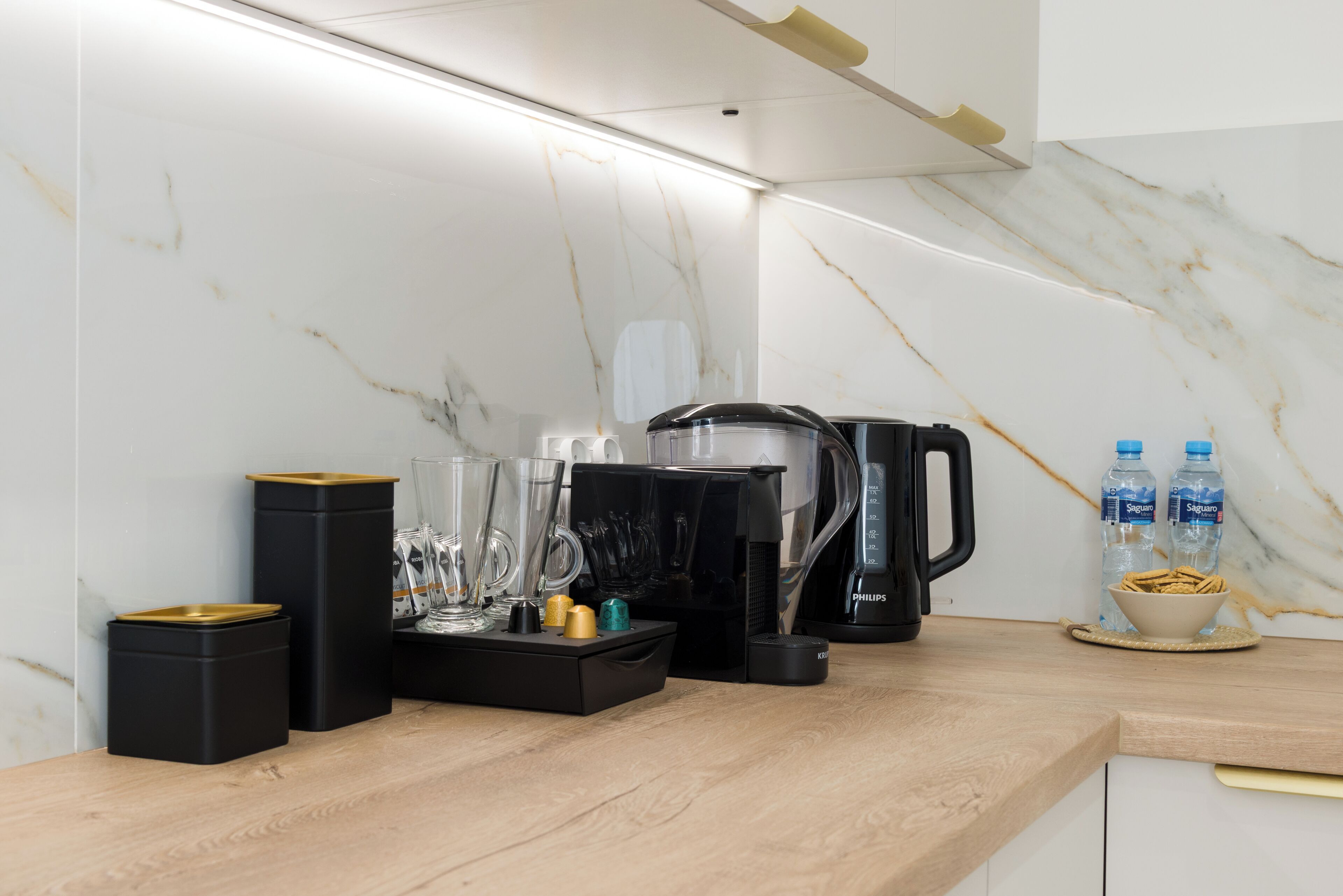 A kitchen with a marble backsplash, a coffee maker, a kettle, and two water bottles on the counter.