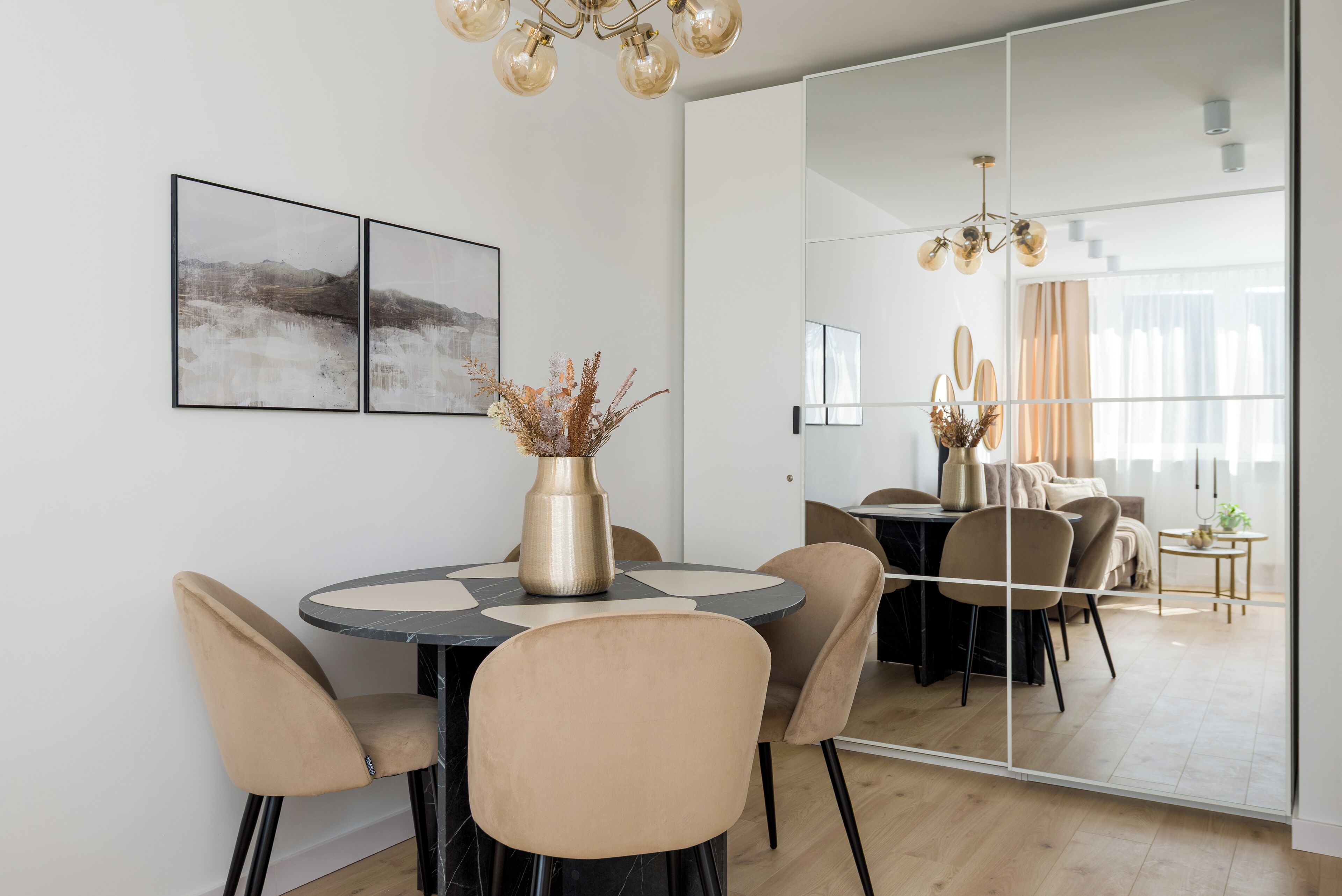 Et moderne spiseområde med et rundt bord, beige stole og en vase med tørrede blomster.