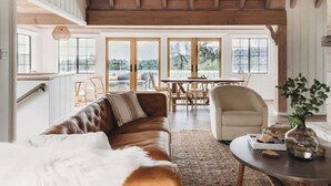 A spacious living room with a leather sofa, a round coffee table, and a view of the outdoors through large windows. - Palisades Point Lakehouse, by @To_Dwell_Here (Lake Arrowhead)
