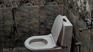 A bathroom with a toilet, shower, and decorative floral tiles. - Spacious 6-bedroom house with WiFi, AC in enchanting Varanasi (Varanasi)