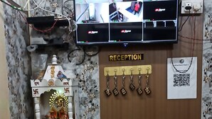 A reception desk with a monitor displaying multiple camera feeds, a small shrine, a QR code for check-in, and a sign indicating the reception area. - Spacious 6-bedroom house with WiFi, AC in enchanting Varanasi (Varanasi)