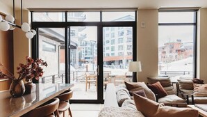 A modern hotel room with a large sliding glass door leading to an outdoor terrace, a sofa set, a dining table, and a vase with dried flowers. - Lift 102 -ski in/out (30 sec. walk, patio to lift) (Park City)