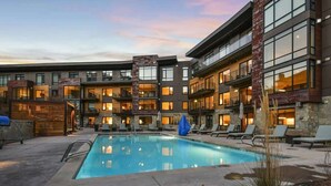 A multi-story hotel with a swimming pool, outdoor seating, and a stone facade. - Lift 102 -ski in/out (30 sec. walk, patio to lift) (Park City)