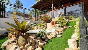 Um jardim paisagístico com diversas plantas e pedras, um caminho de pedra e uma grande janela com vista para o jardim.