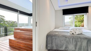 Un dormitorio moderno con una cama grande, vistas a zonas verdes y una escalera de madera que conduce a un espacio exterior.