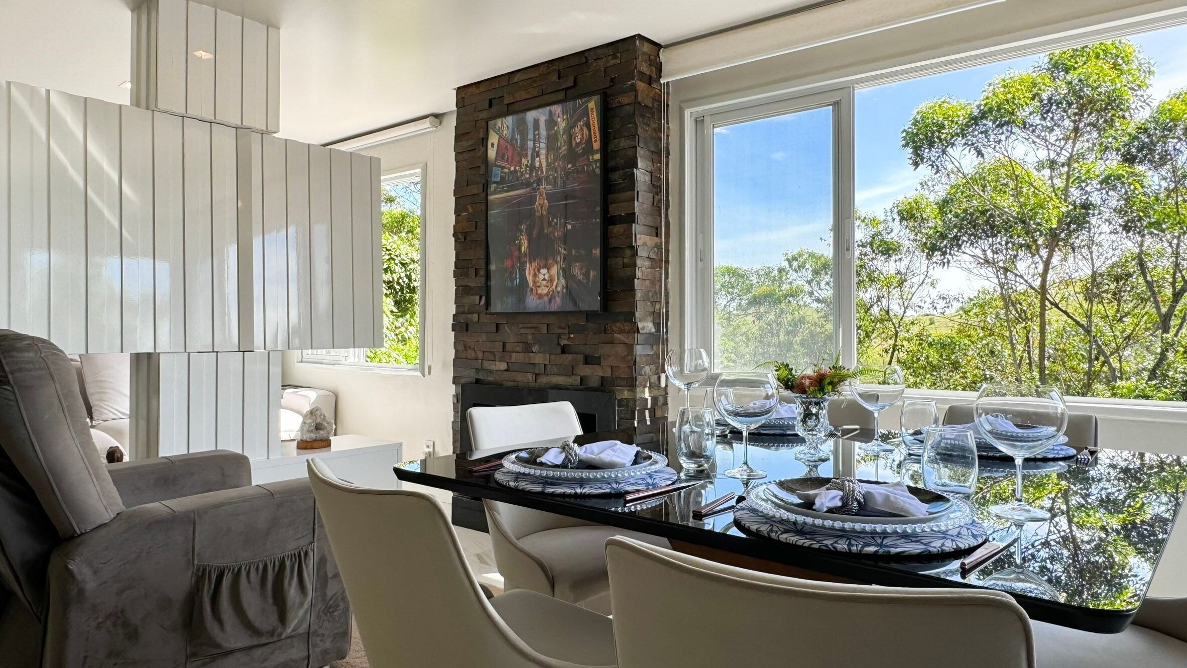 A modern dining area with a glass table, white chairs, and a stone accent wall.