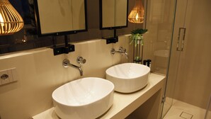 Ein Badezimmer mit zwei runden weißen Waschbecken, einem Spiegel darüber und einer Glasdusche.