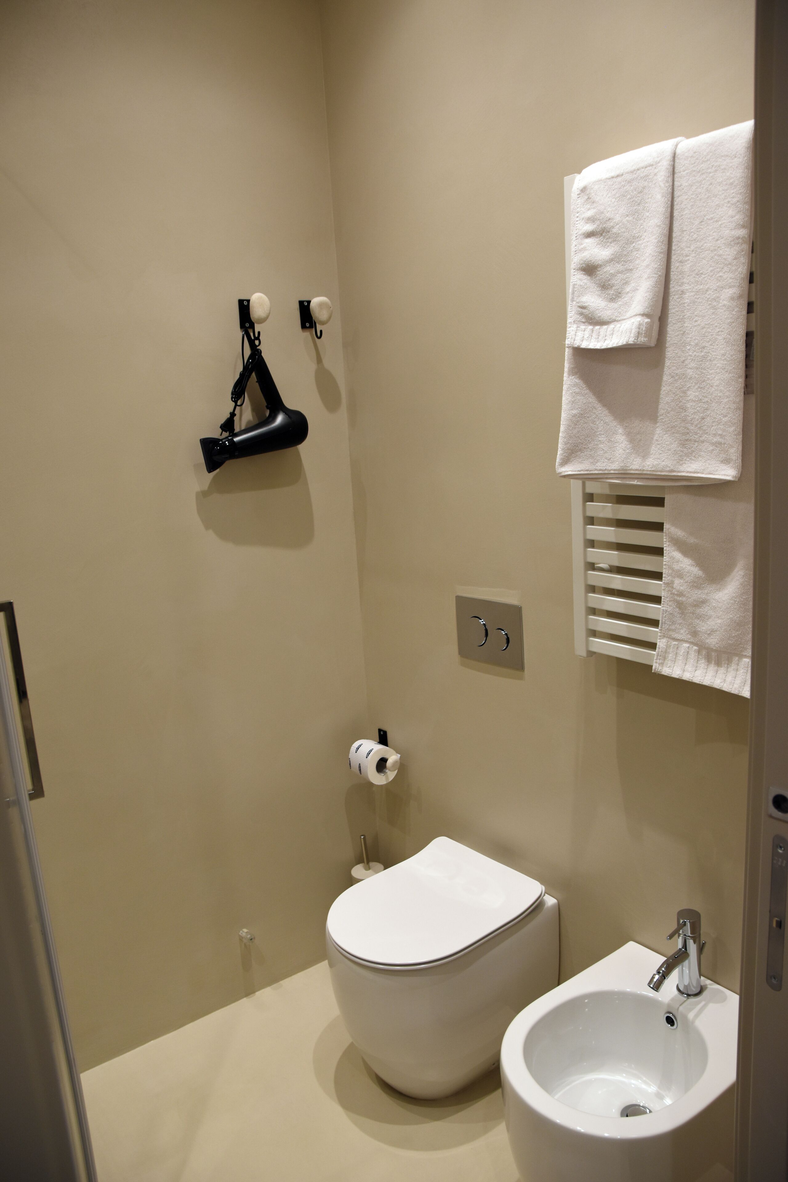 Ein kleines Badezimmer mit Toilette, Bidet, Handtuchhalter und einem an der Wand befestigten Handtuchwärmer.