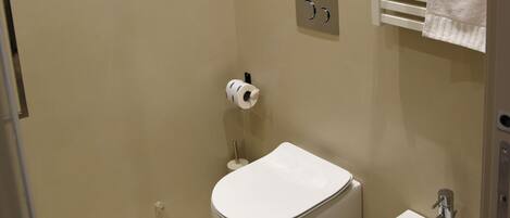 Ein kleines Badezimmer mit Toilette, Bidet, Handtuchhalter und einem an der Wand befestigten Handtuchwärmer.
