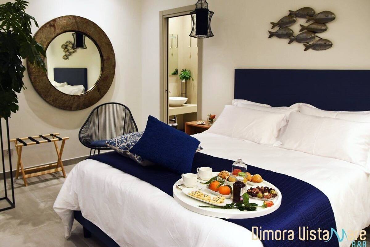 A neatly arranged bedroom with a bed, a bedside table, a tray of breakfast items, a mirror, and a wall decoration.