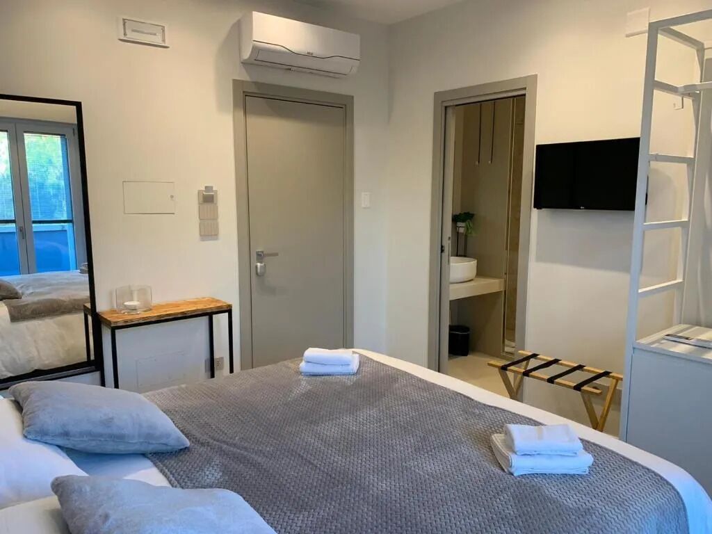 A hotel room with a bed, a small table, a TV, and a bathroom visible through an open door.