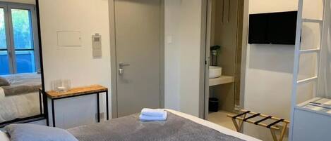 Habitación de hotel con cama, una mesita, televisión y baño visible a través de una puerta abierta.