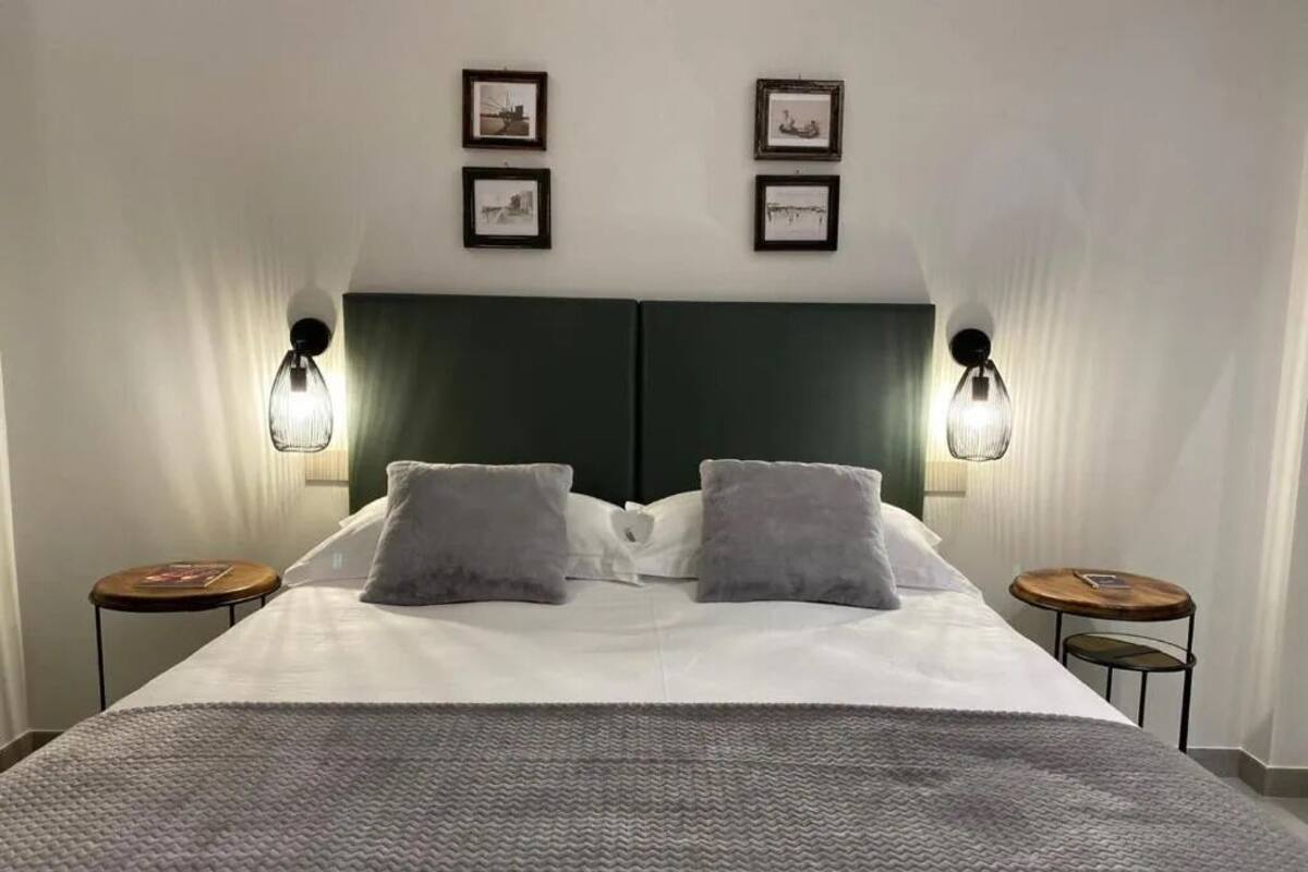 A neatly made bed with a grey blanket, two bedside tables, and wall-mounted lamps.