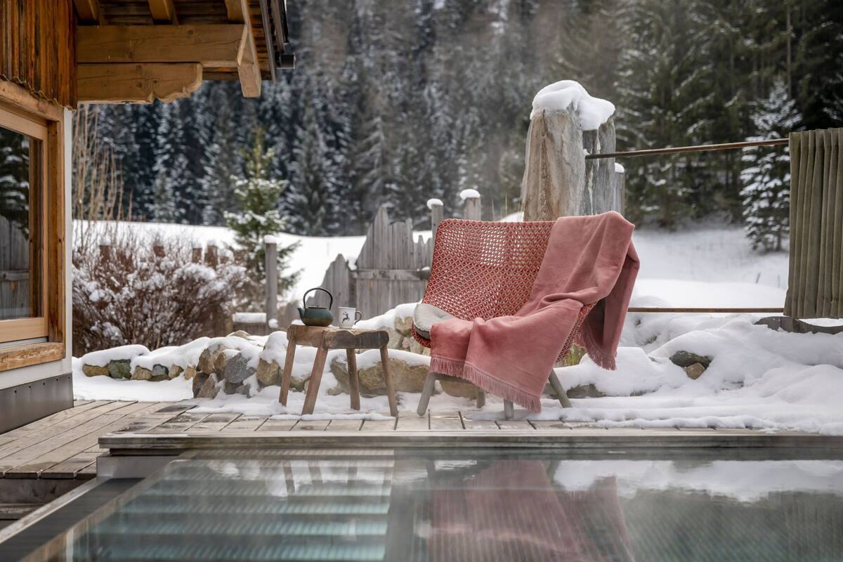A wooden deck with a hot tub, a stone wall, and a red woven chair with a pink blanket.