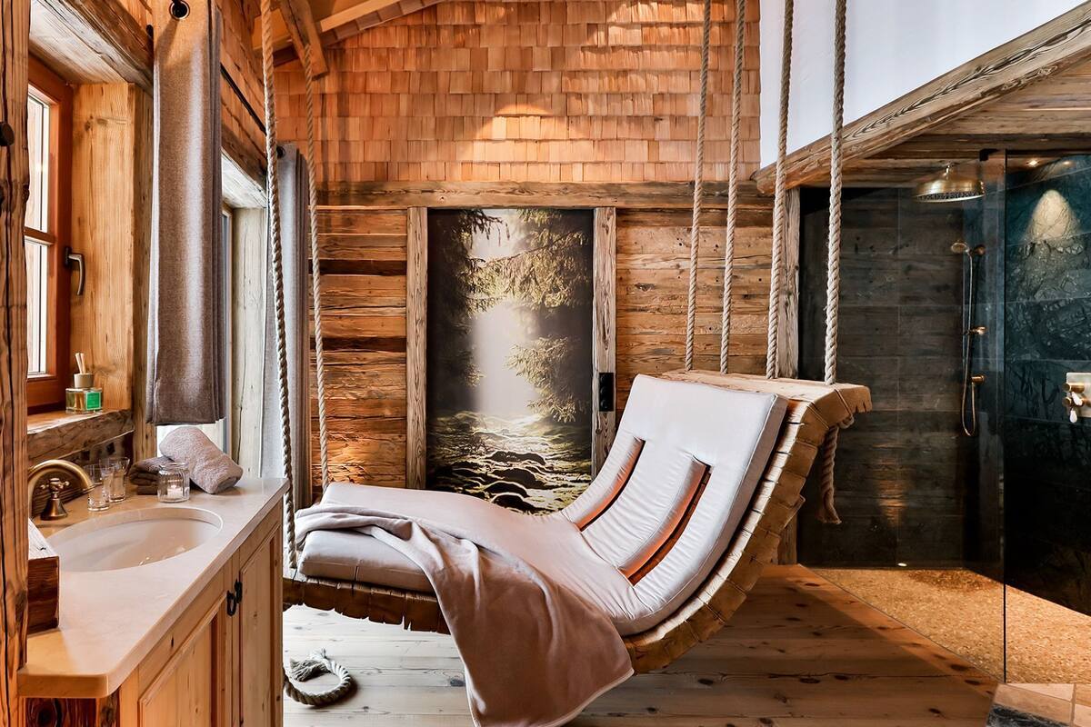 A wooden cabin interior with a hanging chair, a sink, and a shower area.