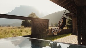 Une terrasse en bois avec une balançoire, donnant sur une piscine, le tout situé dans un cadre montagneux.