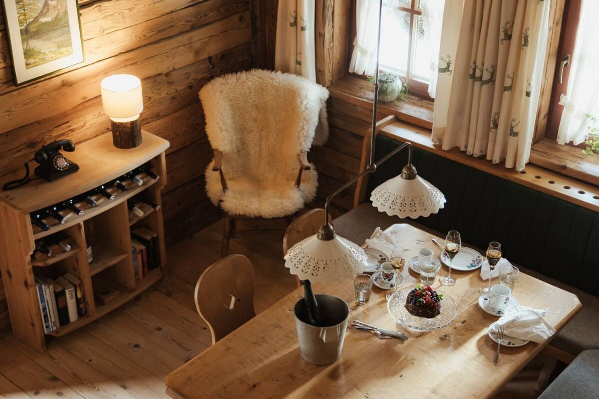 A cozy room with a wooden table set for tea, a chair, a bookshelf, and a lamp.