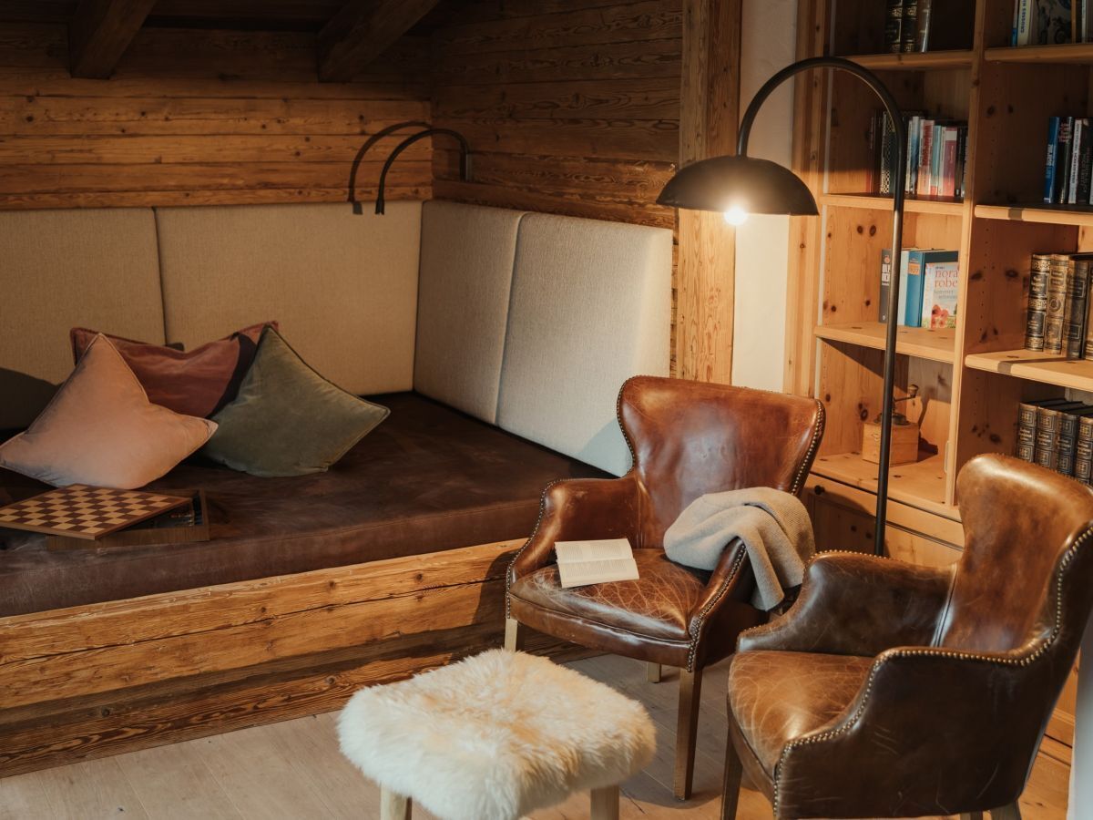 A cozy room with a wooden bench, leather armchairs, a bookshelf, and a fur rug.