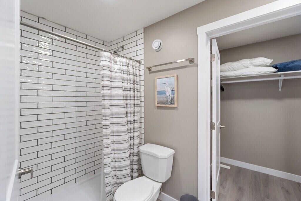A bathroom with a white toilet, a shower with a striped curtain, and a tiled wall.