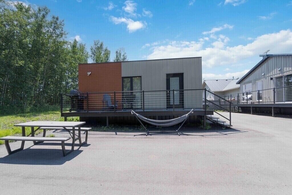 Un bâtiment moderne doté d’une partie en bois et d’une partie en métal, d’un hamac et de tables de pique-nique.
