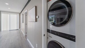 A laundry room with a large circular window, a wall-mounted washing machine, and a dryer. - Modern Home and guest house in peaceful location. (Alberta Beach)