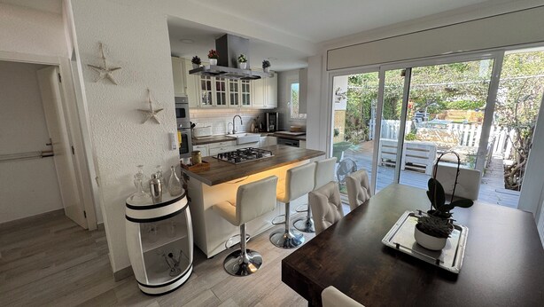 A modern kitchen with white cabinets, a central island, and a dining area with a dark wooden table and white chairs. - HOUSE IN MASNOU NEXT TO BEACH AND TRAIN (El Masnou)