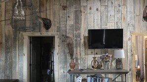 A rustic room with a wooden wall, a flat-screen TV mounted above a wooden table, and a door to the right. - Rustic Comfort Cabins-Anglers Basin with Hot Tub (Amity)