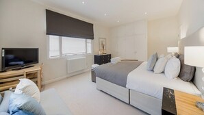 Un dormitorio con cama, televisor, cómoda y ventana con persiana.