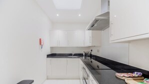 A modern kitchen with white cabinets, a black countertop, and a built-in oven. - Mayfair Oxford Street by Estatesmen (London)