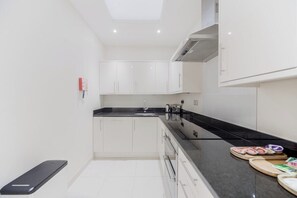 A modern kitchen with white cabinets, a black countertop, and a built-in oven. - Mayfair Oxford Street by Estatesmen (London)