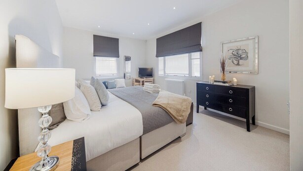 A modern bedroom with a bed, bedside table, dresser, and artwork on the wall. - Mayfair Oxford Street by Estatesmen (London)