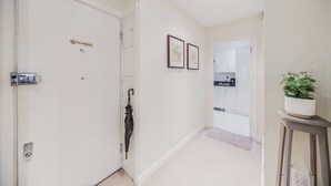 Un pasillo con una puerta cerrada, un letrero de prohibido fumar, cuadros en la pared y una planta en una mesita.
