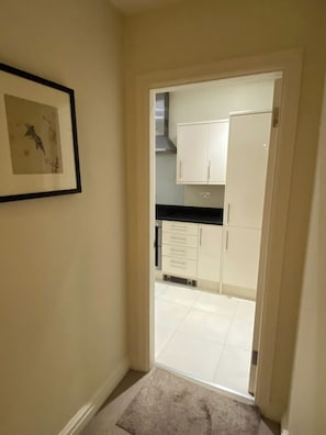 Un couloir menant à une cuisine avec des meubles blancs et un tableau encadré accroché au mur.