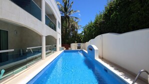 Ein Swimmingpool mit klarem, blauem Wasser, umgeben von einem weißen Gebäude mit Balkonen und Palmen.