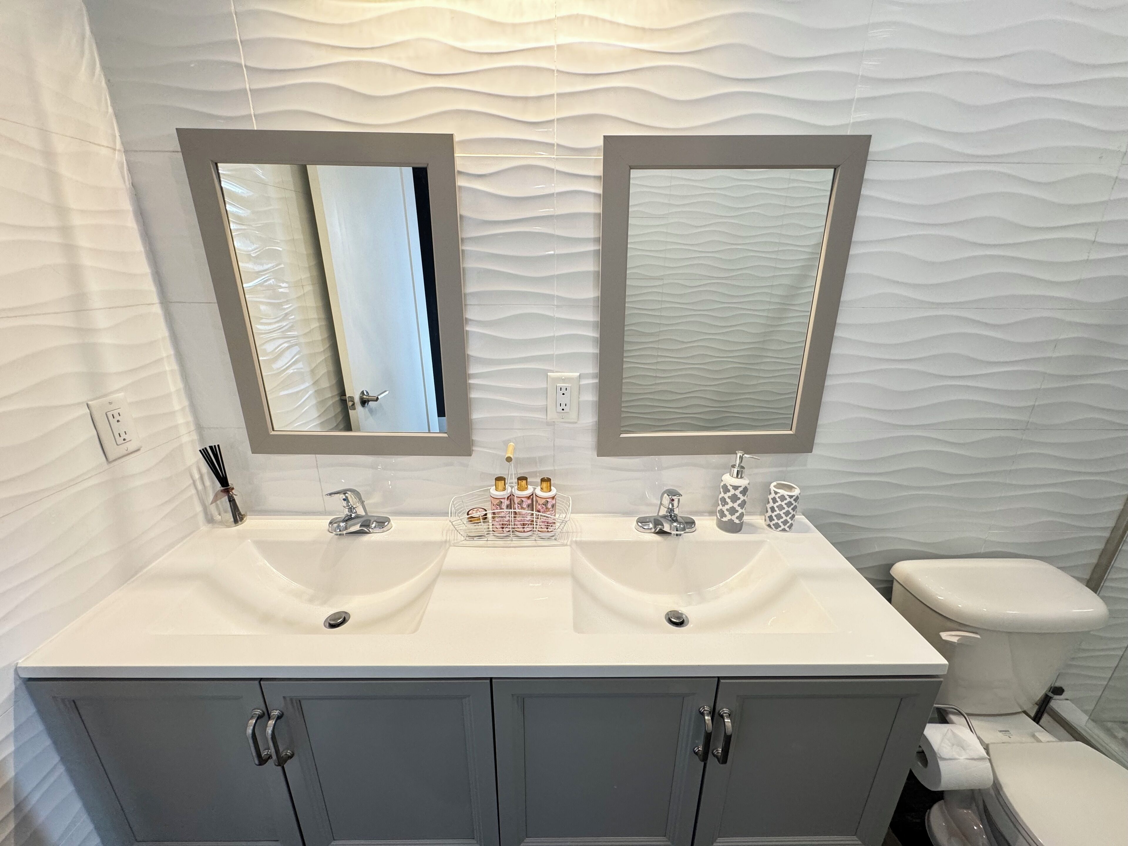 Un baño con tocador doble, dos espejos, un inodoro y pared con diseño.