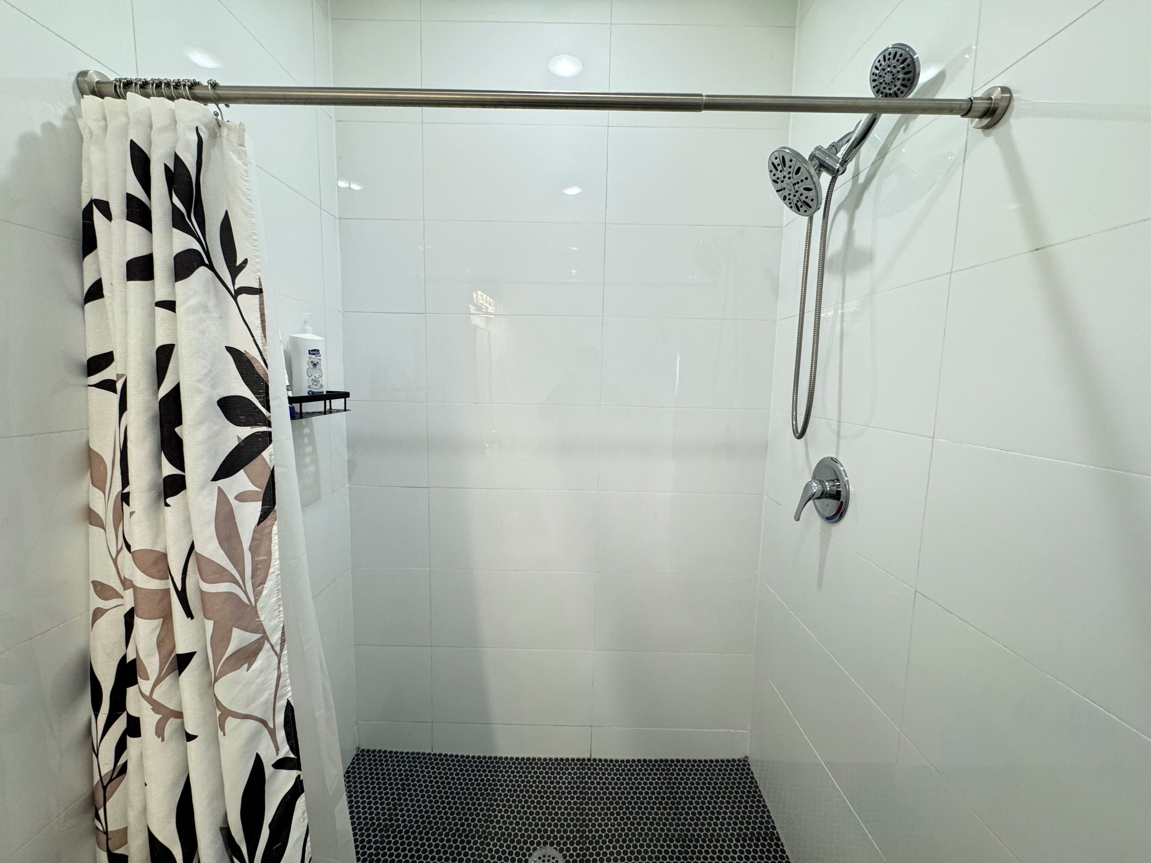 Zona de ducha con una barra metálica, un cabezal de ducha de mano y un grifo instalado en la pared.