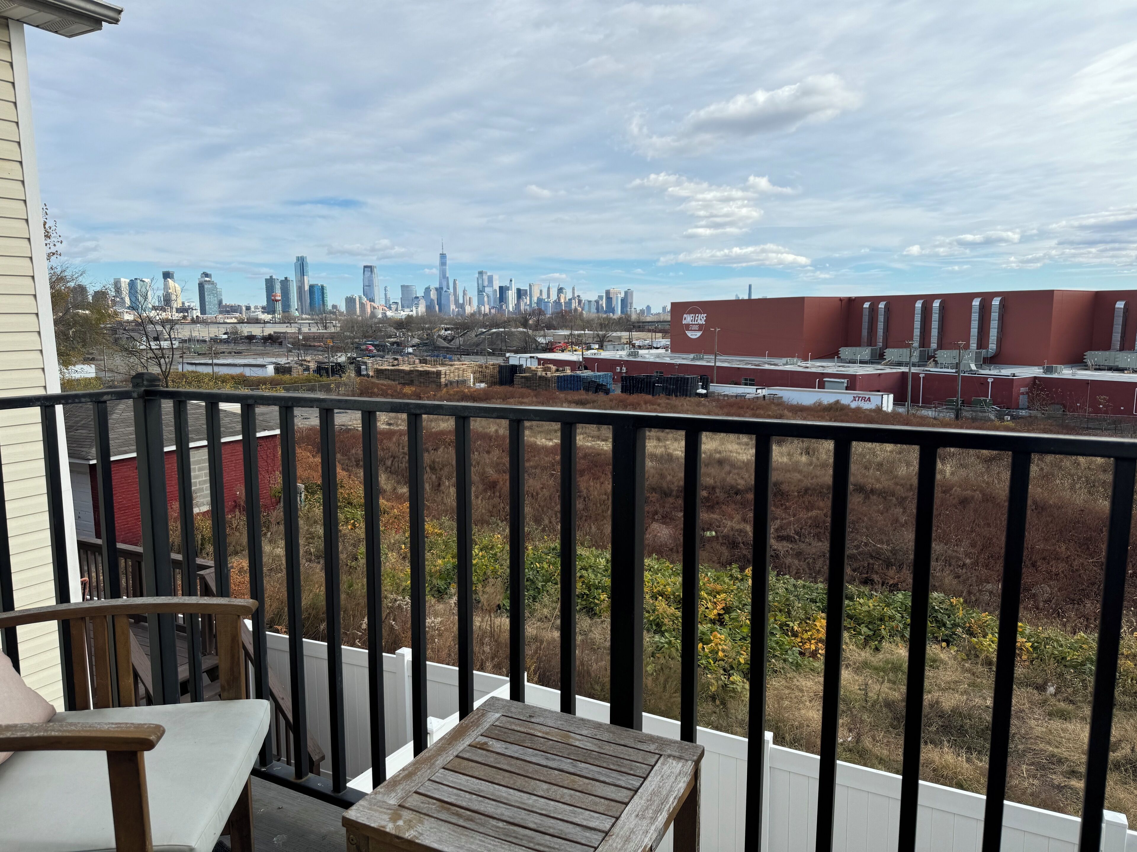 A balcony with a view of a city skyline, a red building, and a white fence.